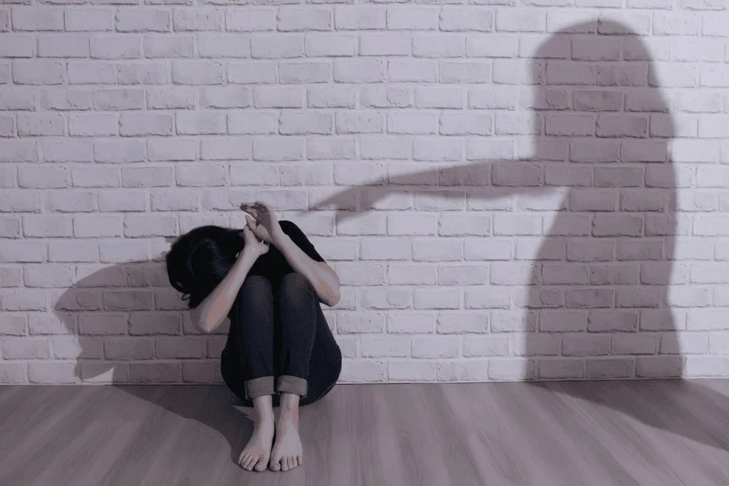 Personne recroquevillée contre un mur avec une ombre menaçante symbolisant les blessures émotionnelles et le traumatisme