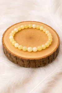 Bracelet en calcite jaune en perles, posé sur un rondin en bois sur fond blanc doux.