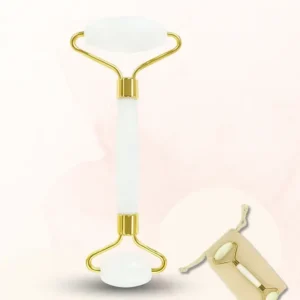 Roller facial en jade blanc avec finitions dorées, présenté avec sa pochette sur fond rose poudré.