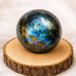 Sphère en labradorite naturelle polie posée sur un support en bois, reflets irisés bleus et dorés
