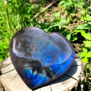 Cœur en Labradorite posé sur un rondin de bois, pierres précieuses lumineuses.