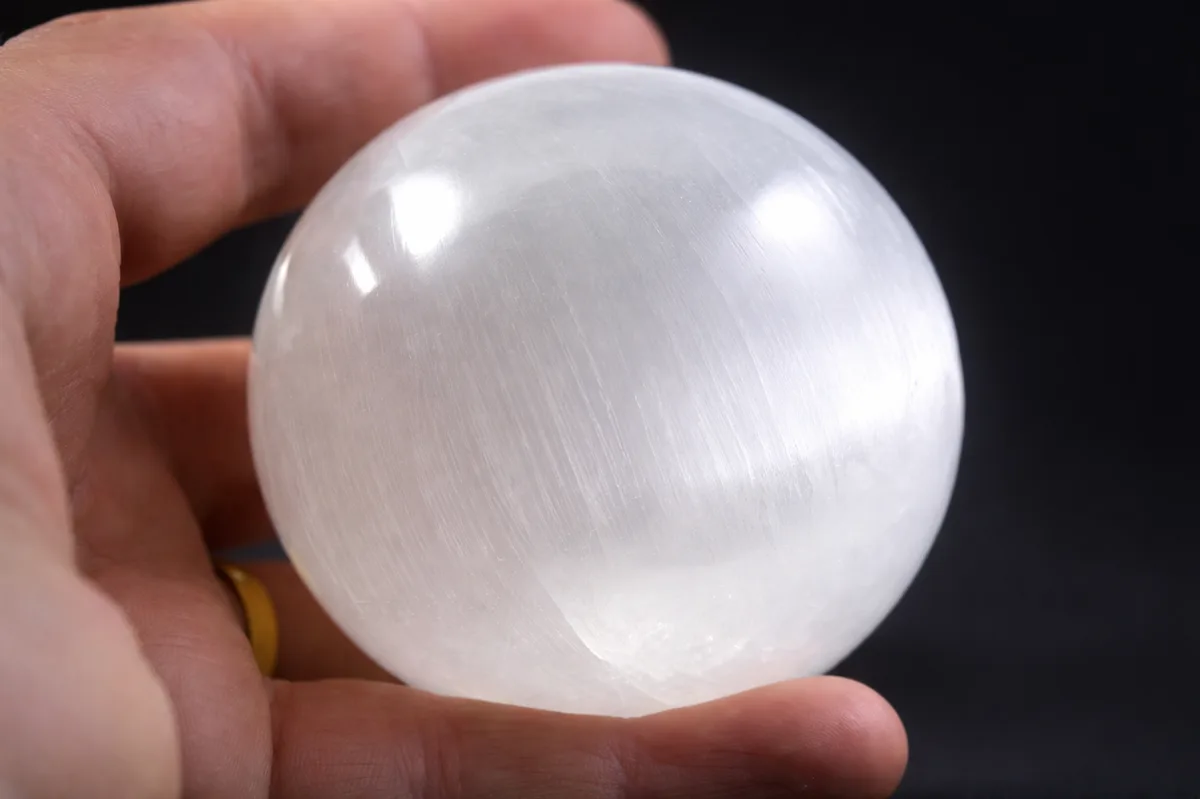Sphère en sélénite 80 mm tenue en main, pierre naturelle blanche utilisée en lithothérapie et méditation
