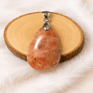 Pendentif pierre de soleil en pierre naturelle posé sur un rondin de bois