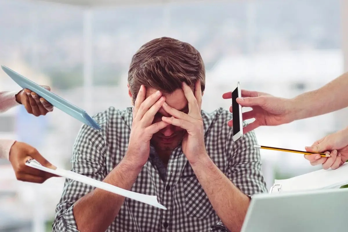 Homme épuisé et stressé au travail, au bord du burn-out, entouré de nombreuses sollicitations professionnelles