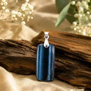 Pendentif œil de faucon bleu rectangulaire présenté sur du bois avec des fleurs blanches.